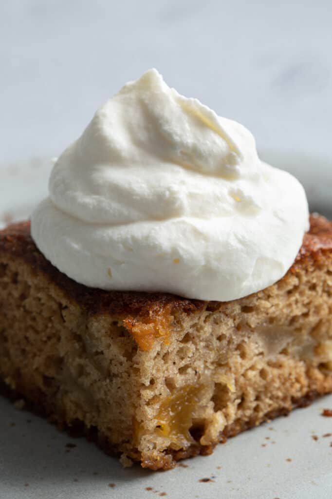 A close up shot of a slice of fruit cocktail cake topped with whipped cream.