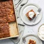 a sheet pan of fruit cocktail cake with two slices cut out and placed onto plates with forks and whipped cream