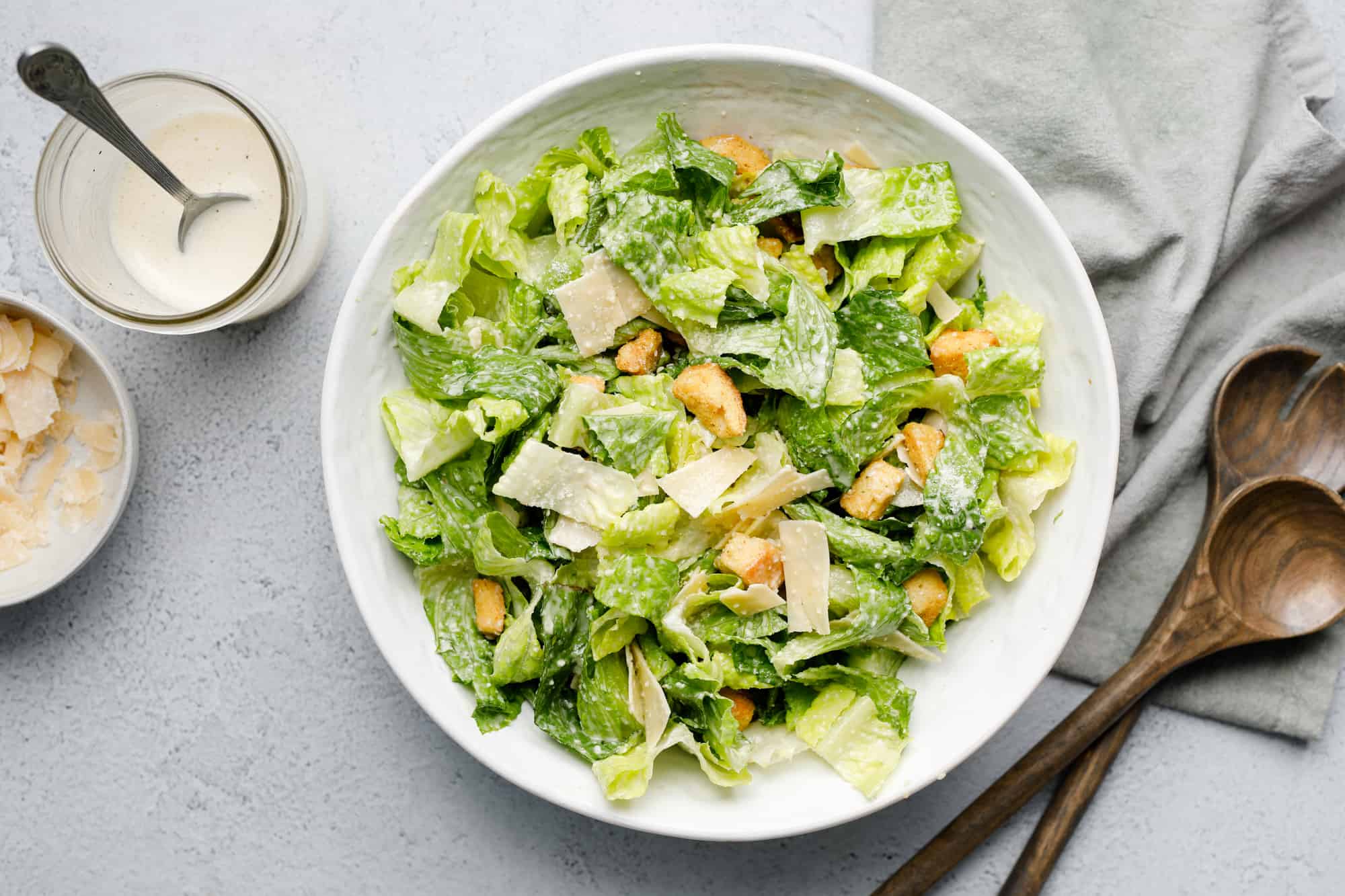 overhead view of a bowl of Caesar salad with tongs and dressing on the side