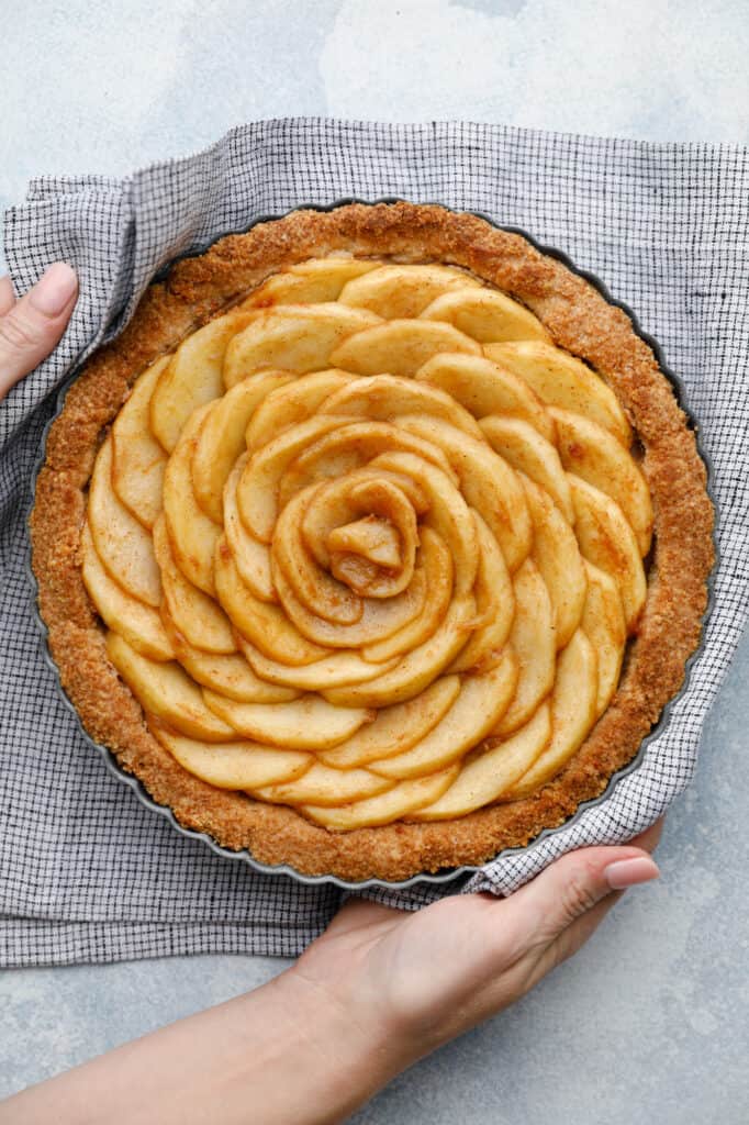 Overhead view of an apple tart with spiraled apples fresh out of the oven being held with two hands an a kitchen towel