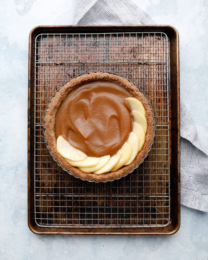 An overhead view of an apple tart being assembled on a wire rack in a cookie sheet pan