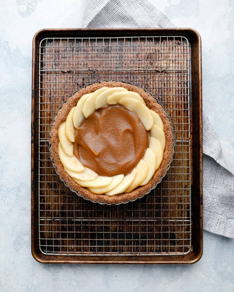 An overhead view of an apple tart being assembled on a wire rack in a cookie sheet pan