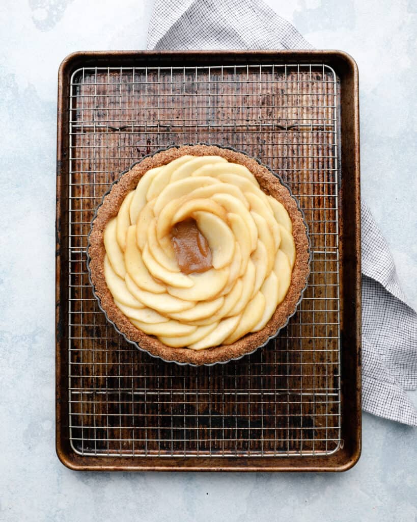 An overhead view of an apple tart being assembled on a wire rack in a cookie sheet pan
