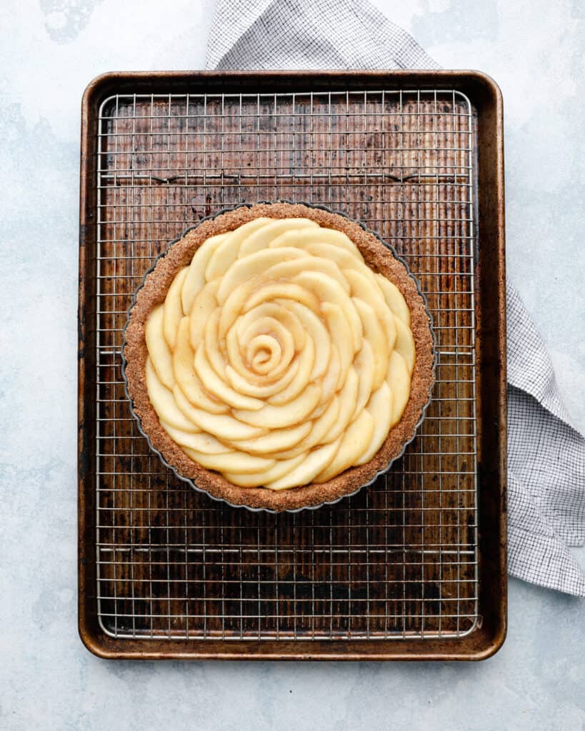 An overhead view of an apple tart being assembled on a wire rack in a cookie sheet pan