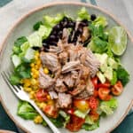 overhead view of a salad with shredded pork, lettuce, tomatoes, avocado and black beans