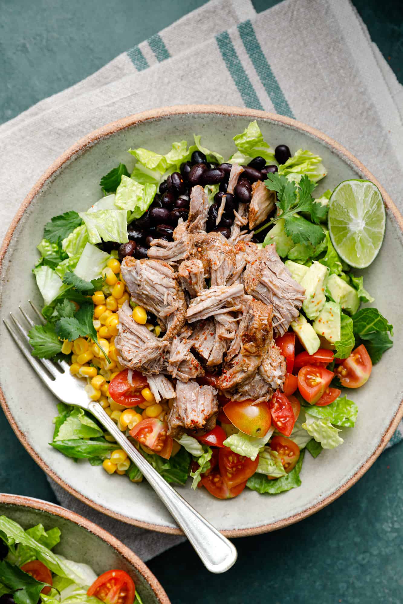 overhead view of a salad with shredded pork, lettuce, tomatoes, avocado and black beans