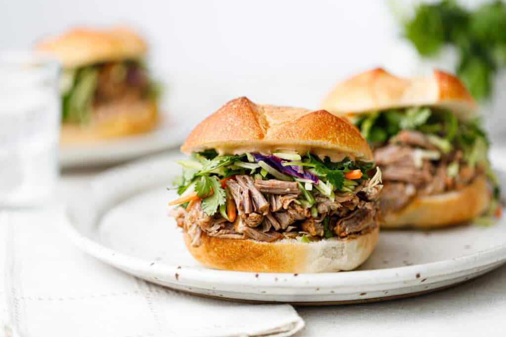 Head on shot of a pulled pork sandwich with broccoli slaw on a white plate