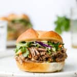 Head on shot of a pulled pork sandwich with broccoli slaw on a white plate