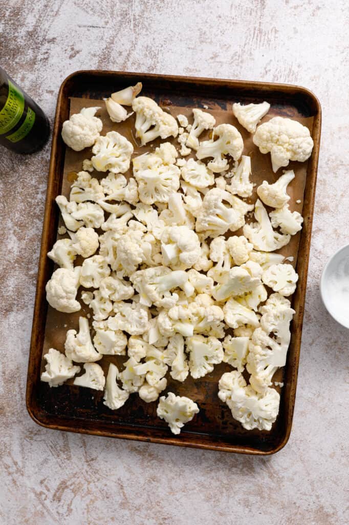 overhead view of a baking pan with cauliflower florets tossed in olive oil and salt
