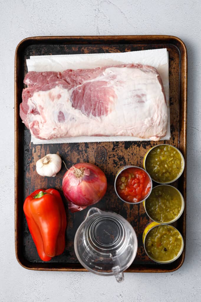 ingredients for green chile pork stew including pork loin, garlic, red onion, red pepper, Rotel, and green chiles