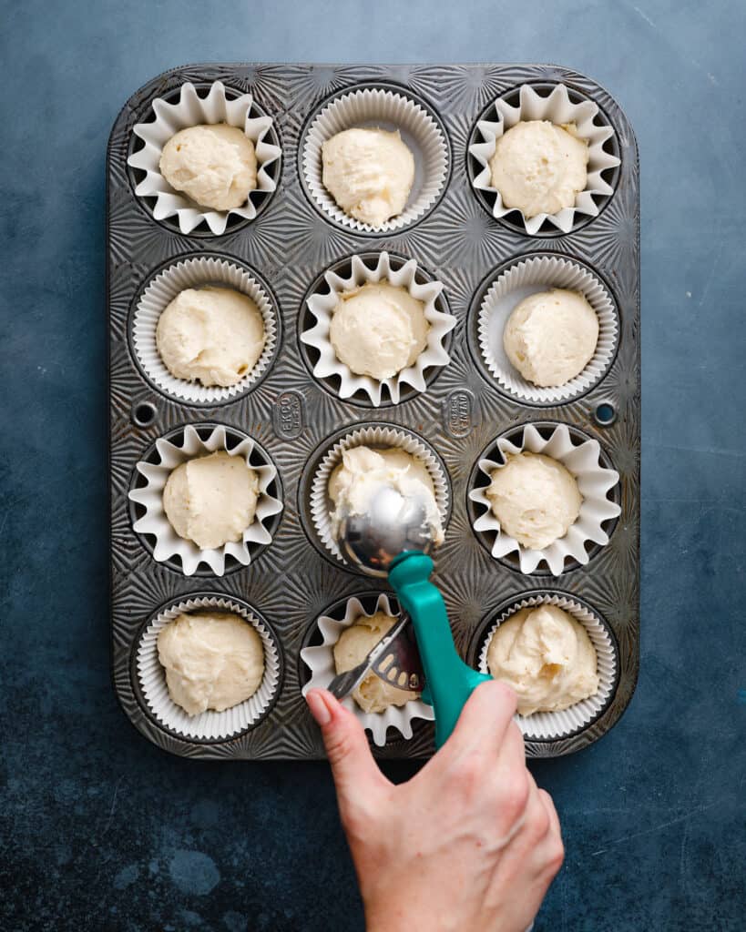measuring out scoops of snickerdoodle muffin batter into a muffin tin