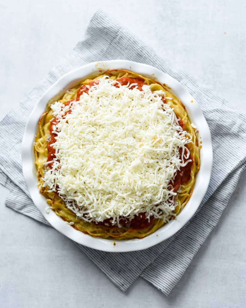 spaghetti pie topped with fresh grated cheese before being put into the oven