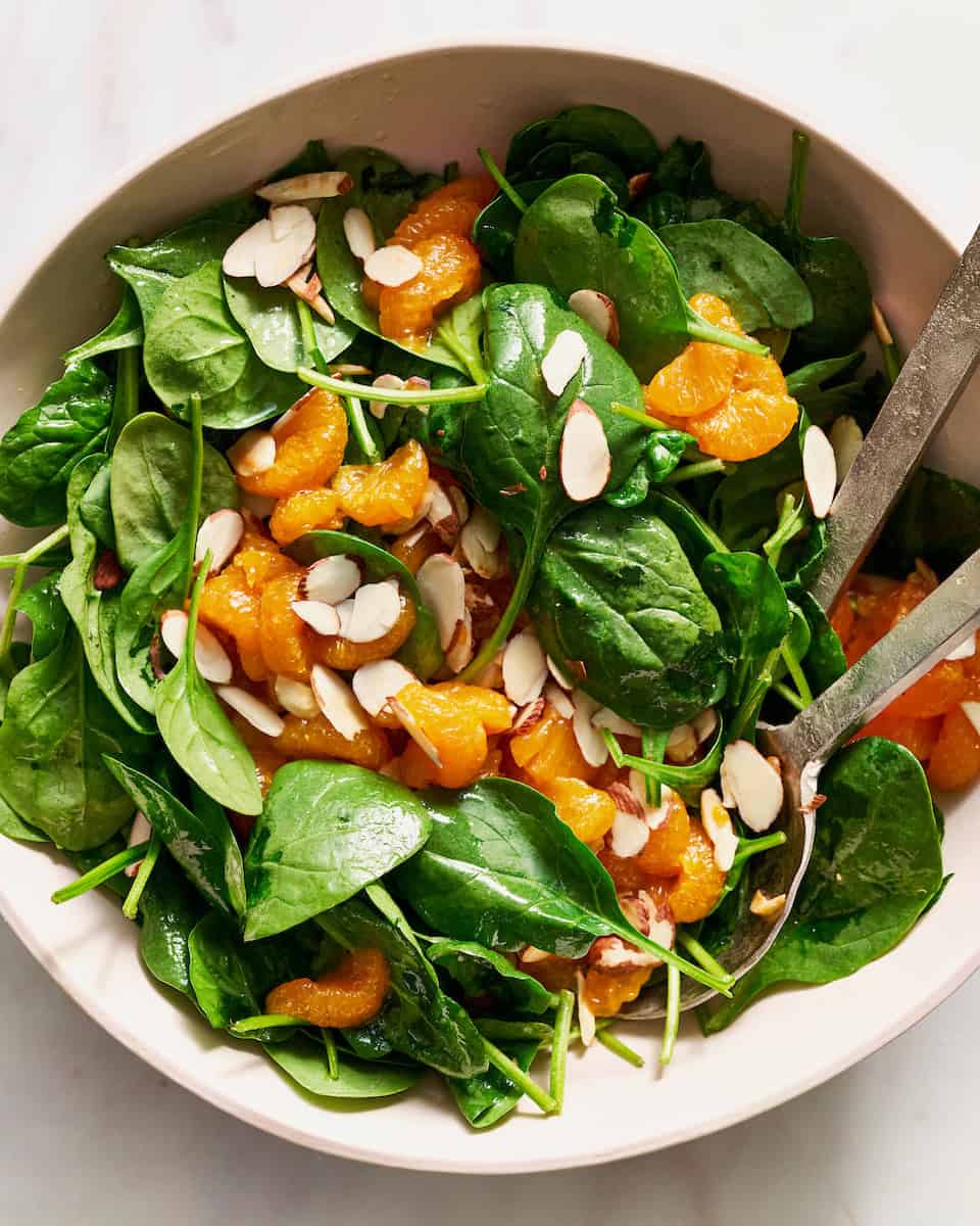 salad being served in a large family style bowl with tongs
