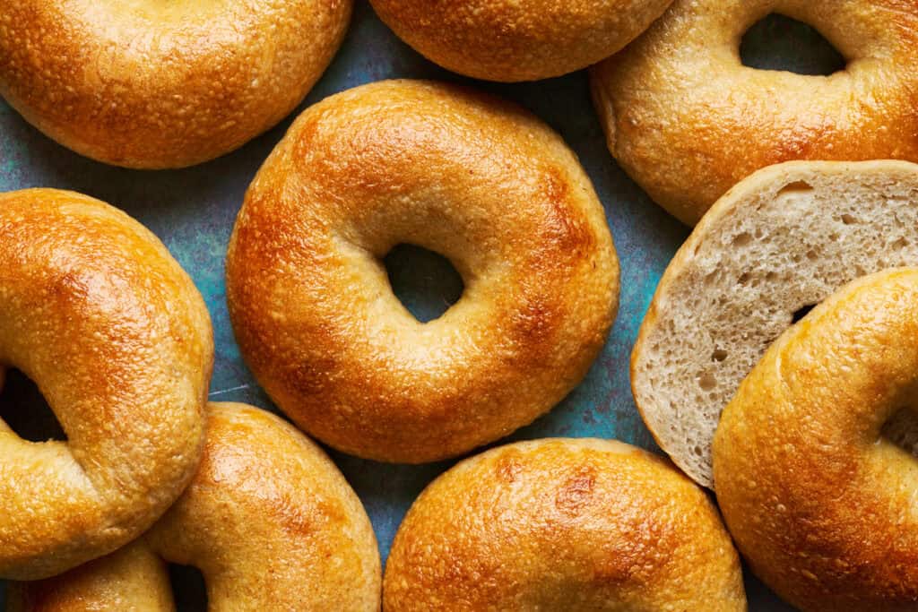overhead view of crispy browned homemade bagels with one sliced to show interior texture