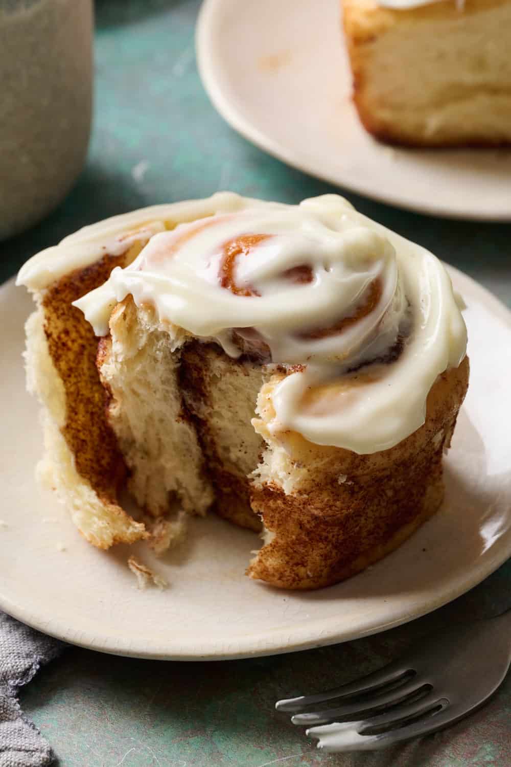 A cinnamon roll on a plate with a bite taken out and glossy frosting on top