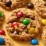 Side angle view of M&M, peanut butter, oatmeal cookies on a yellow background