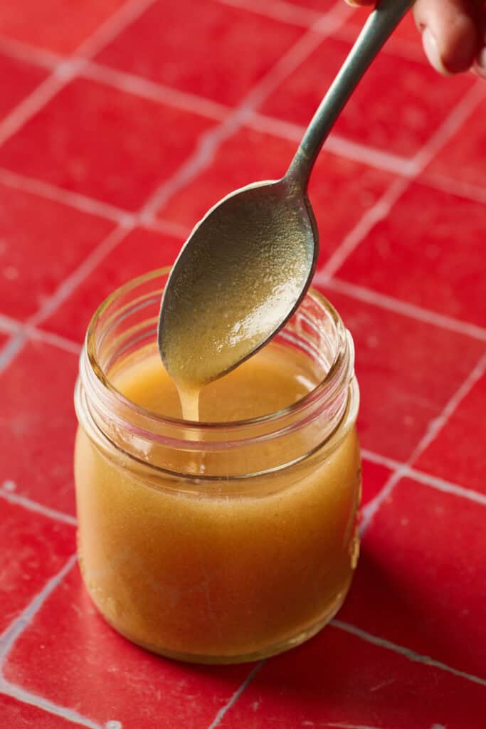 apple cider dressing in a jar with a spoon being lifted out