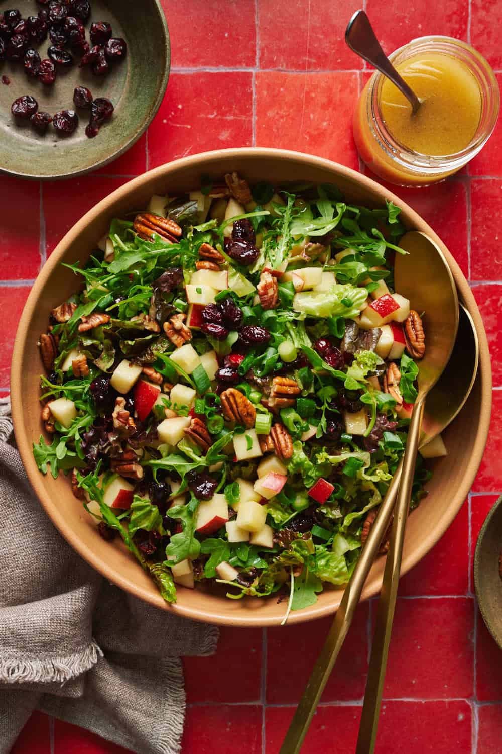 Arugula salad with apples, pecans, cranberries and scallions in a large salad bowl with tongs.