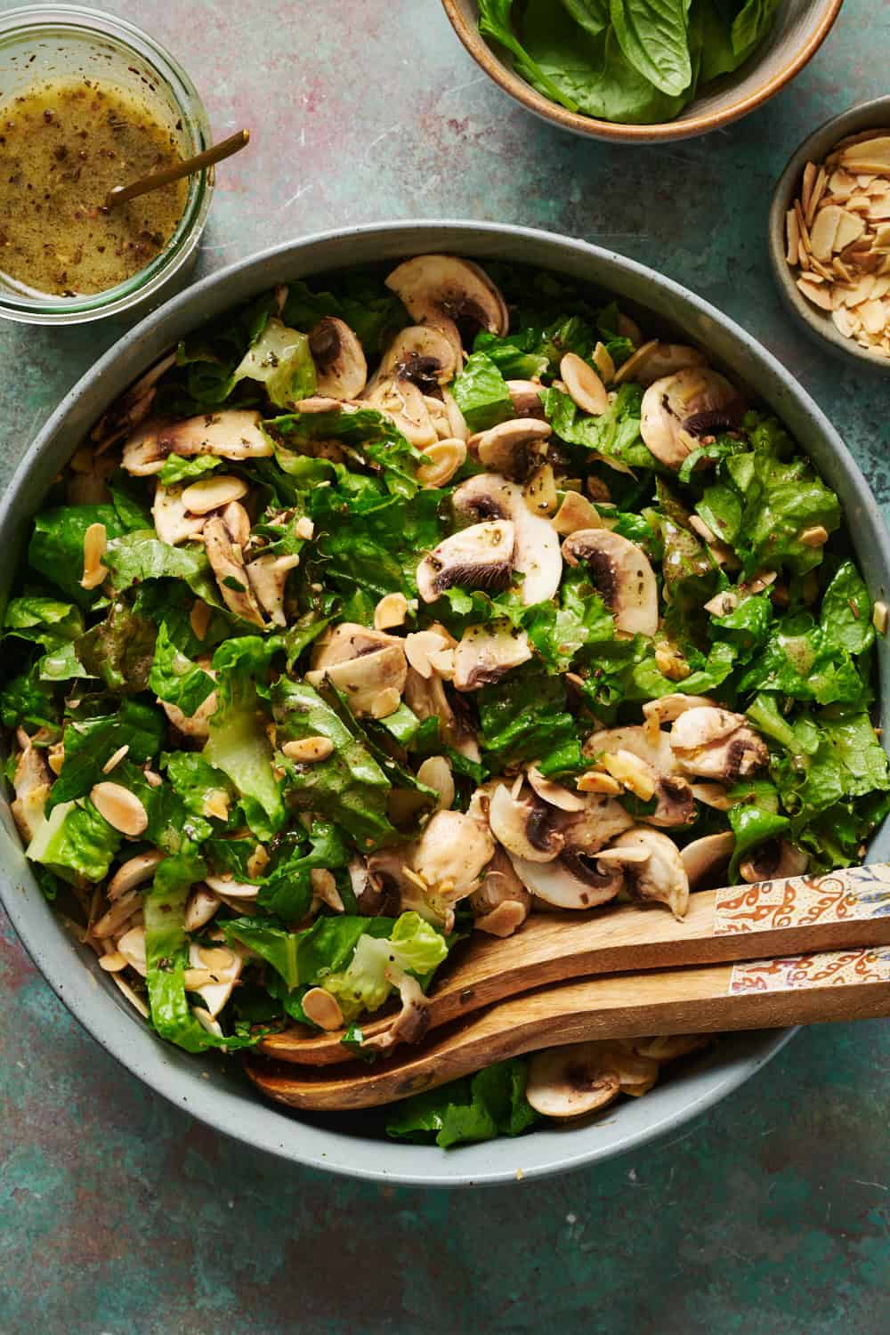 overhead view of a salad with mushrooms in a large bowl with salad tongs and dressing on the side