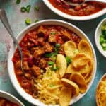 overhead view of a bowl of steak chili topped with chips and cheese
