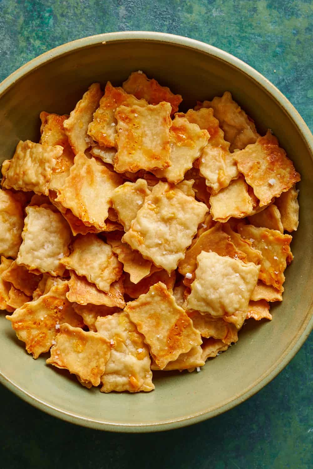 overhead view of a bowl of golden sourdough discard crackers on a green background