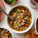 overhead view of a bowl of pressure cooker beef barley soup with bread on the side