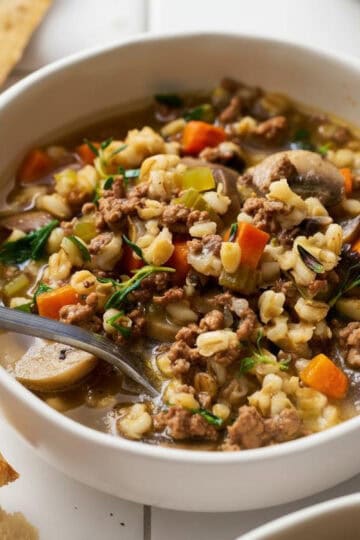 overhead view of a bowl of pressure cooker beef barley soup with bread on the side