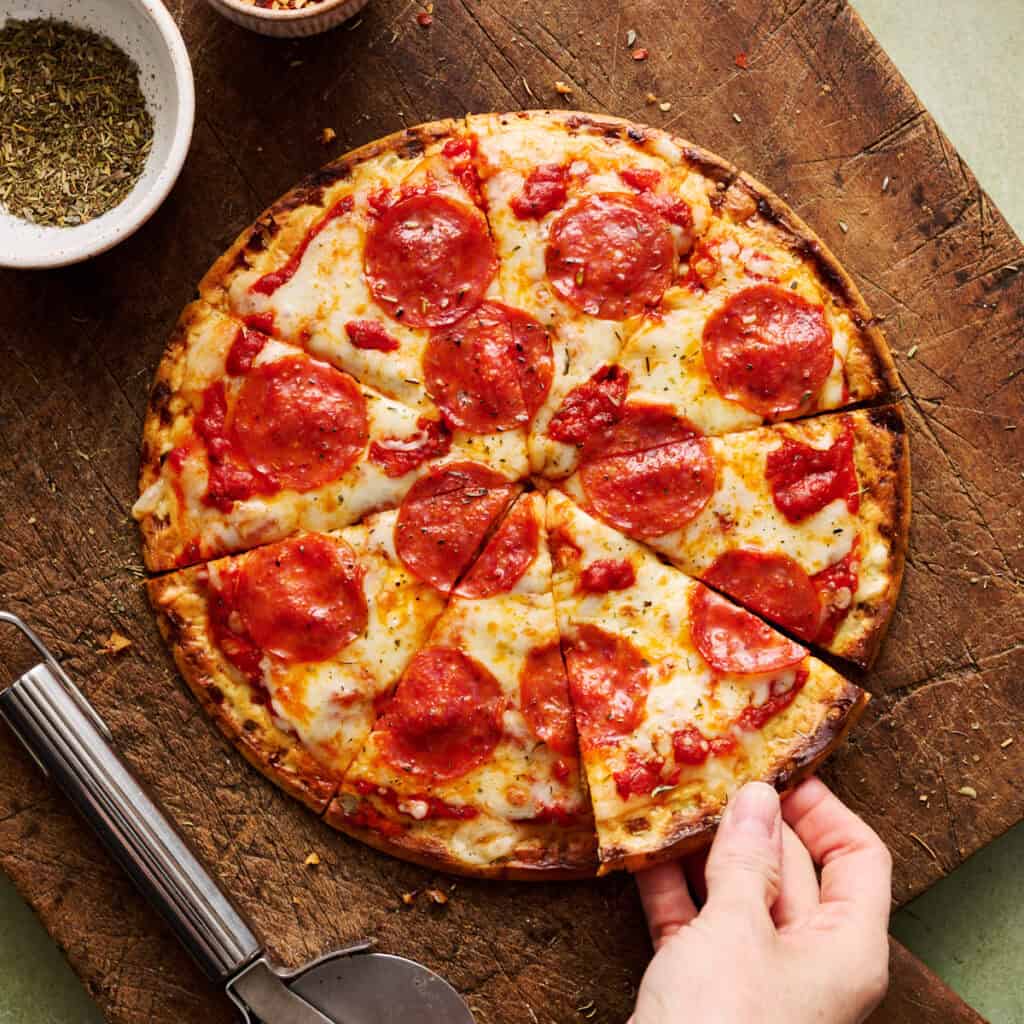 a sliced pizza with cottage cheese crust and a hand grabbing a slice