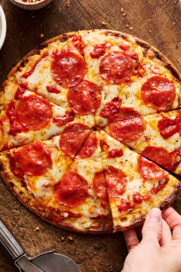 a sliced pizza with cottage cheese crust and a hand grabbing a slice