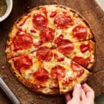 a sliced pizza with cottage cheese crust and a hand grabbing a slice