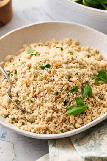 Fonio pilaf in a serving bowl garnished with herbs