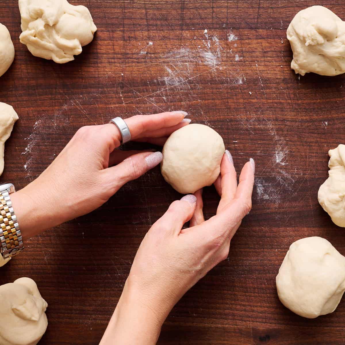 two hands rolling the dough into a smooth ball on a work surface