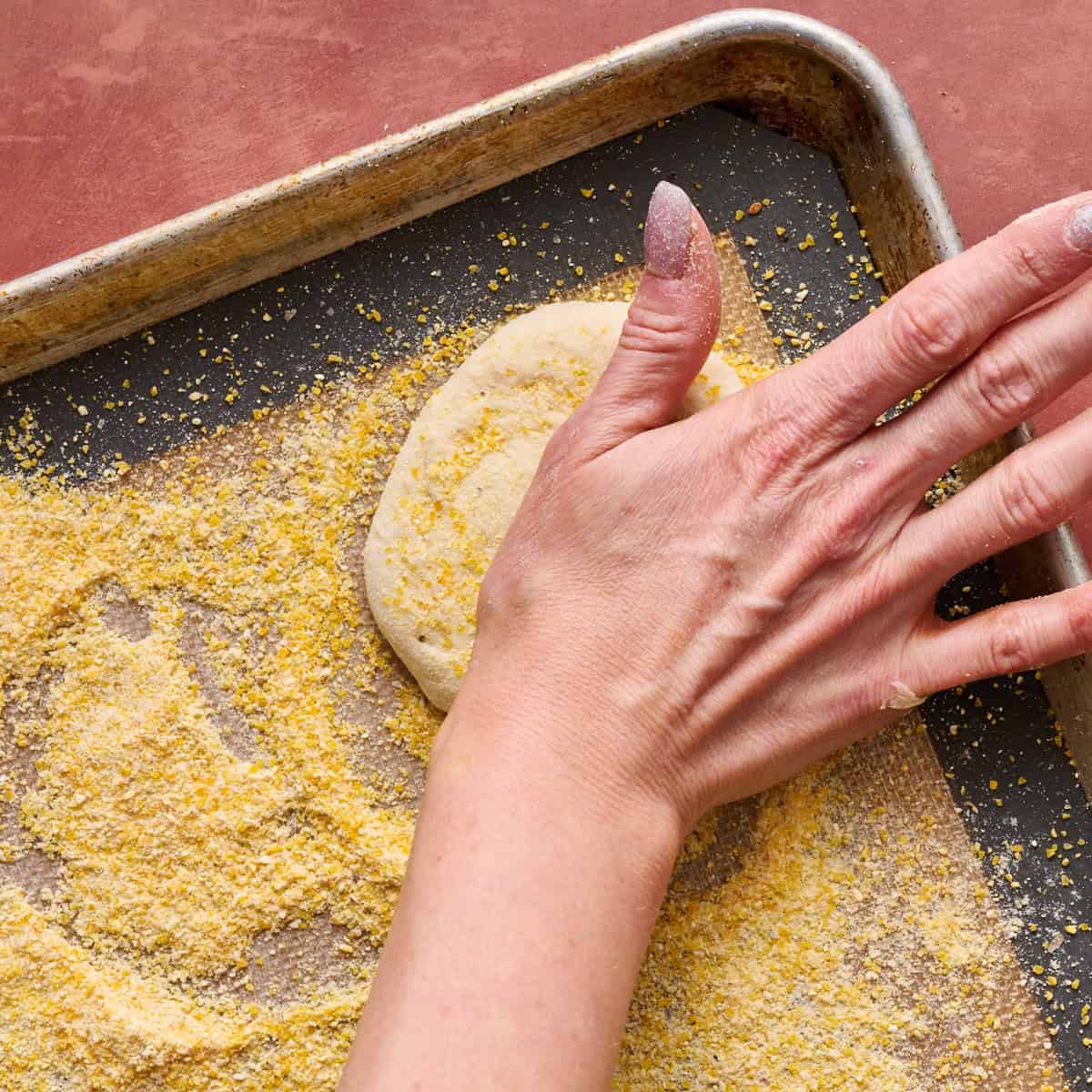 a hand pressing down on a piece of dough to form the english muffin