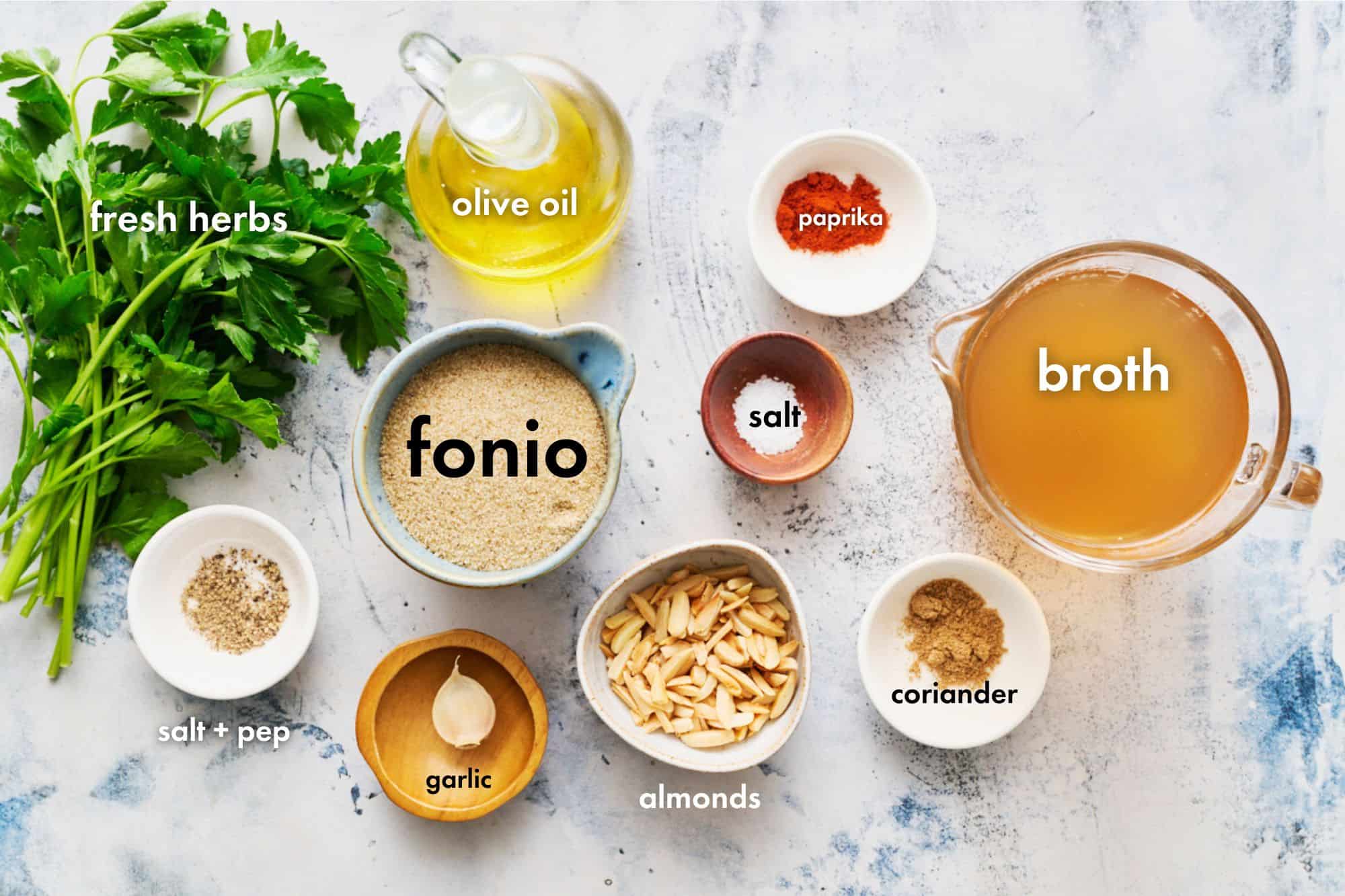 ingredients for making fonio pilaf including broth, herbs, olive oil, garlic, almonds, salt, pepper and spices
