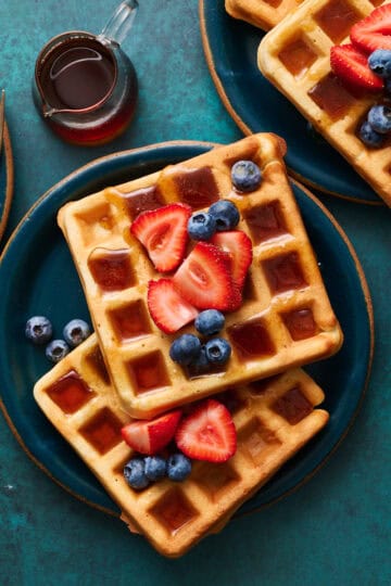 sour cream waffles on plates topped with berries and maple syrup