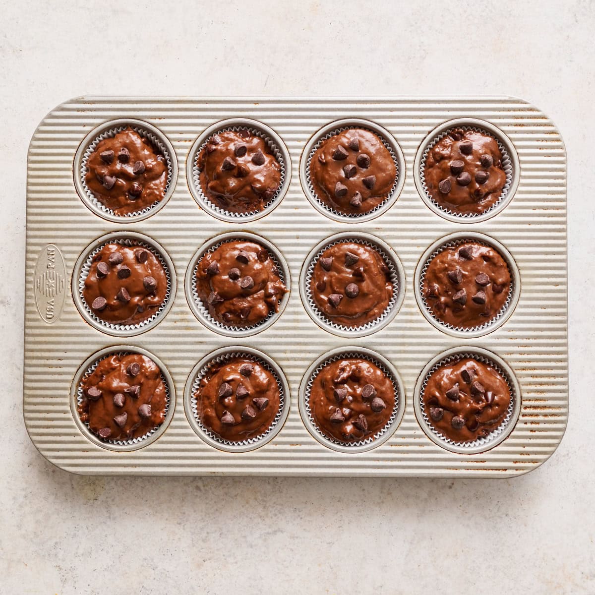 batter scooped into a a 12-muffin tin with extra chocolate chips on top