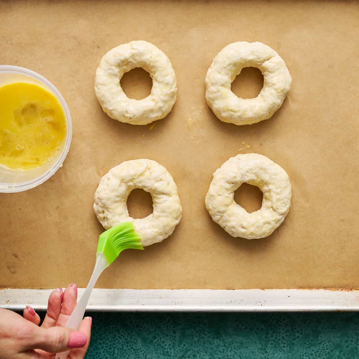 bagels on parchment paper being brushed with egg wash