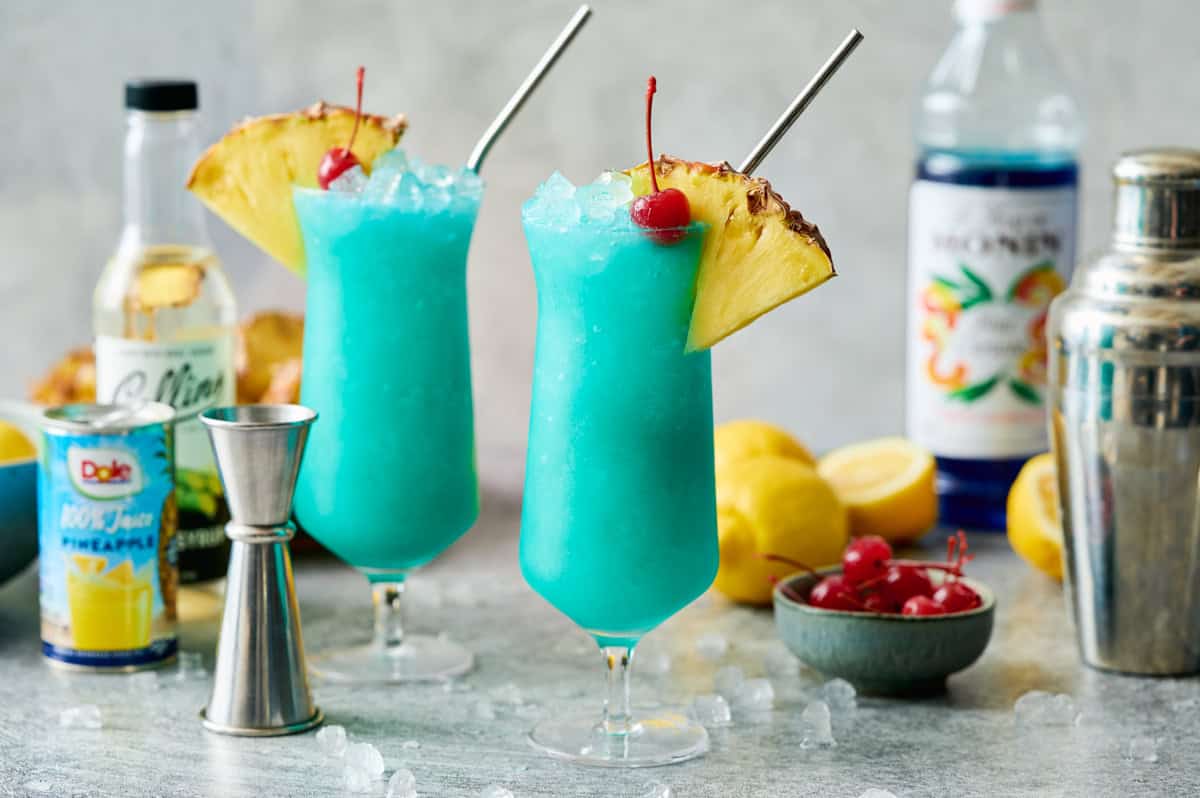 blue hawaii mocktails in hurrican glasses with ice, straws, pineapple and cherries