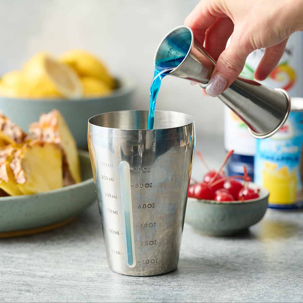 pouring blue curacao syrup into a cocktail shaker