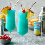 Two hurricane glasses filled with blue hawaii mocktail and ice