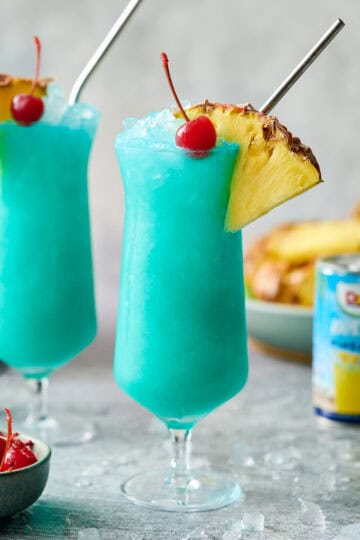 Two hurricane glasses filled with blue hawaii mocktail and ice