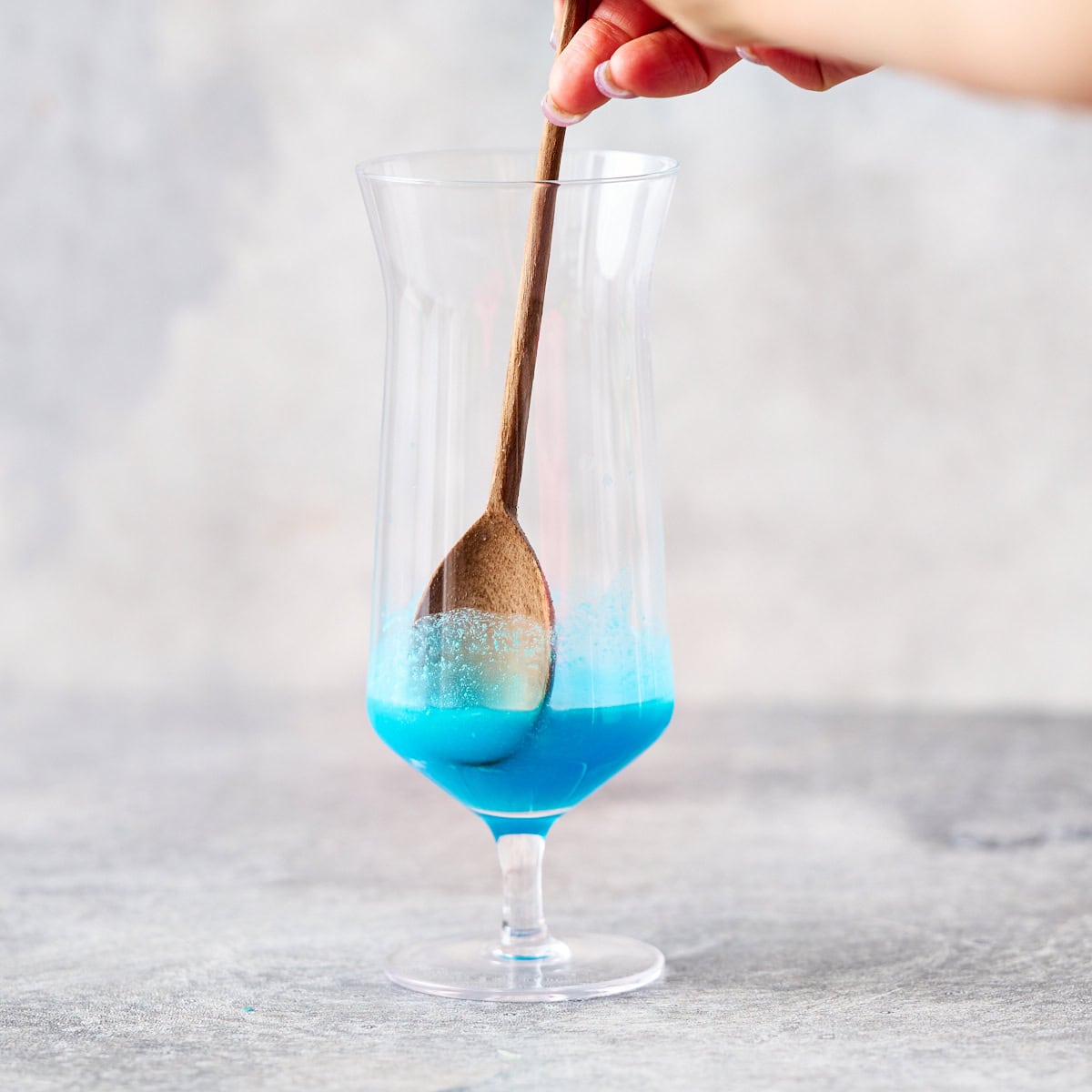 lime juice, coconut cream and blue curacao being stirred in a hurricane glass