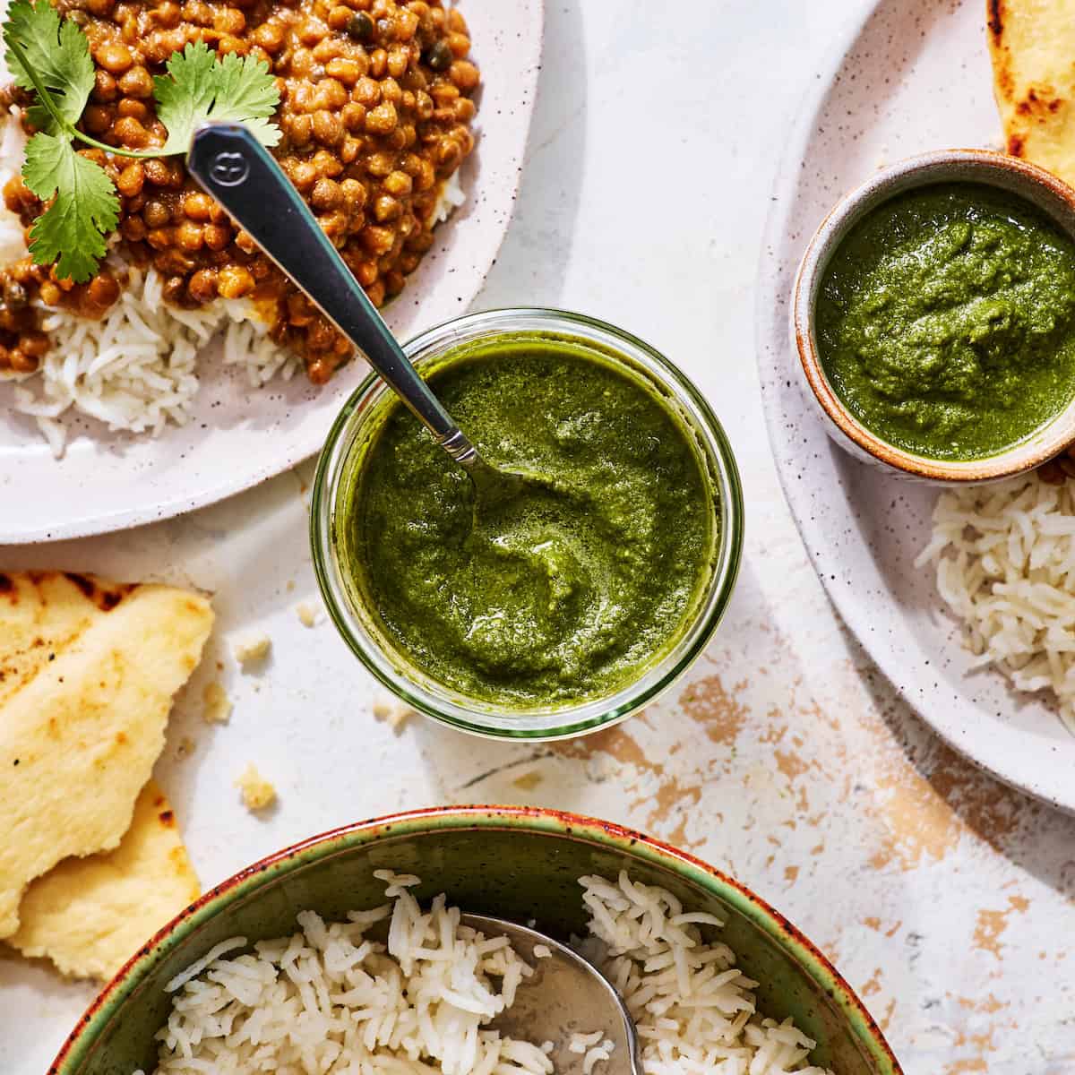 green chutney in a glass jar with naan bread and servings of curry
