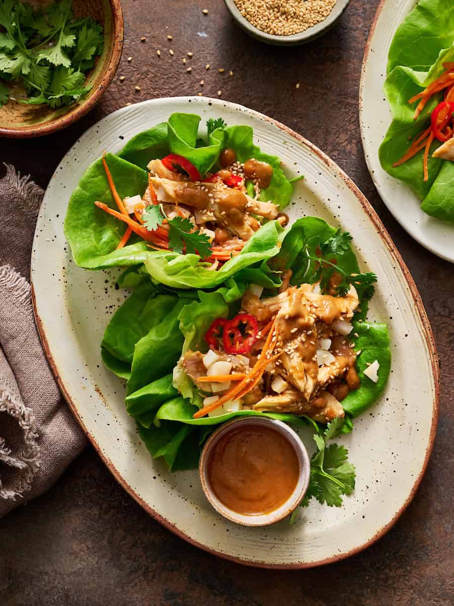 Lettuce Wraps on a plate filled with shredded chicken topped with homemade peanut sauce and fresh peppers, carrots and sesame seeds