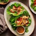 Overhead view of a plate filled with chicken lettuce wraps with extra peanut sauce on the side