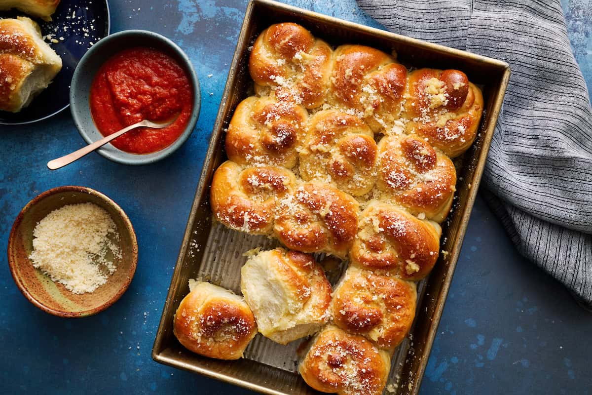 sourdough discard garlic knot rolls in a baking pan with marinara and parmesan
