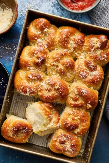 sourdough discard garlic knot rolls in a baking pan with marinara and parmesan