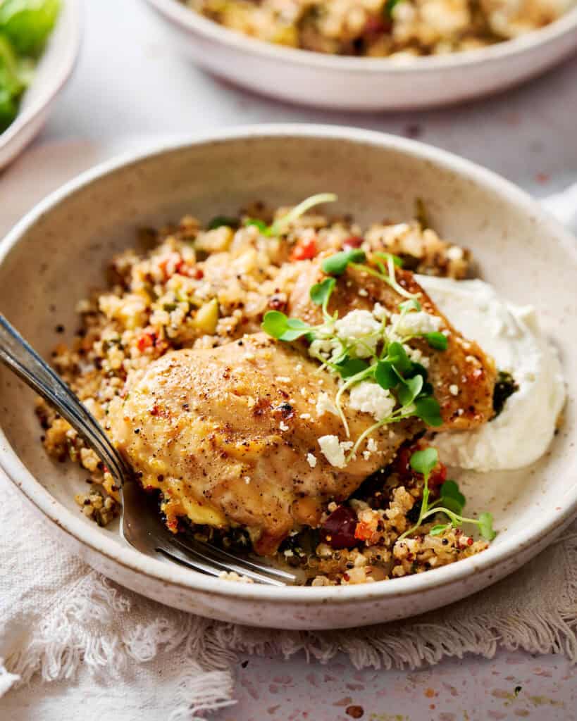 One pan Mediterranean chicken quinoa bake plated in a dish with golden brown chicken thighs, crumbled feta cheese