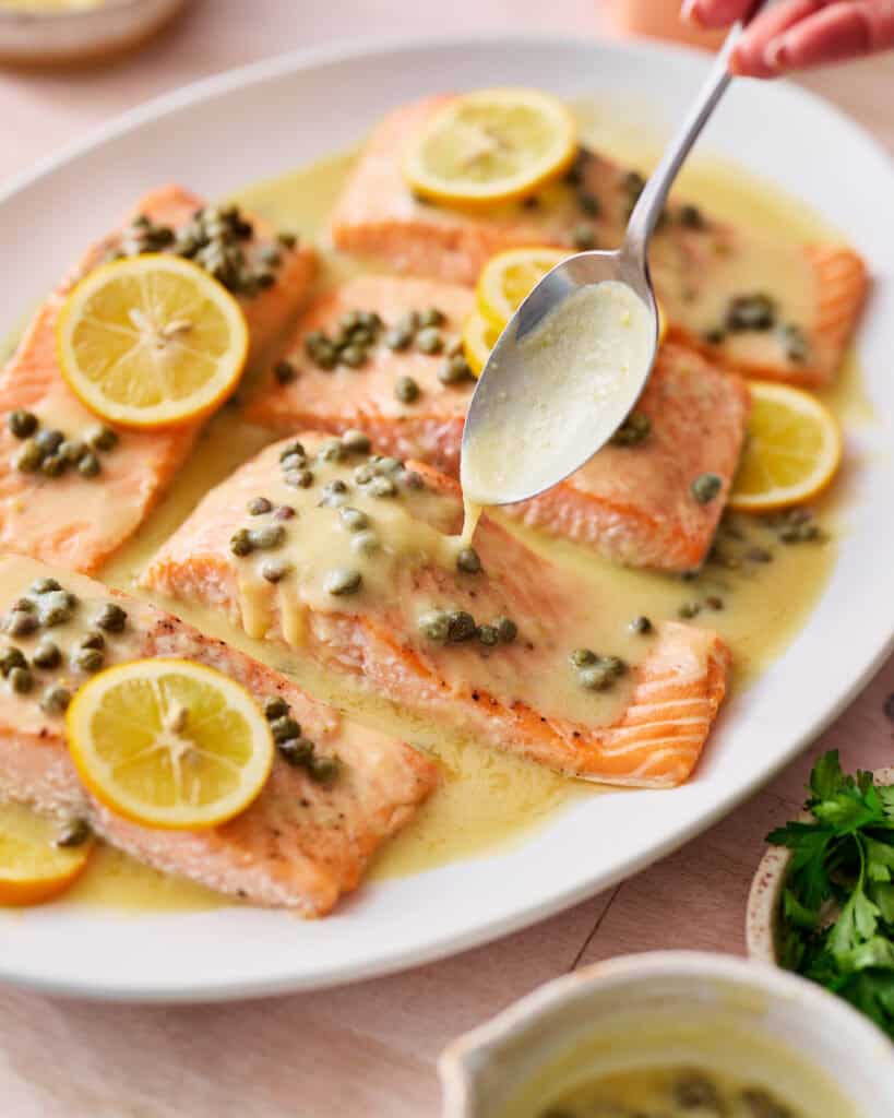 spooning piccata sauce on salmon filets