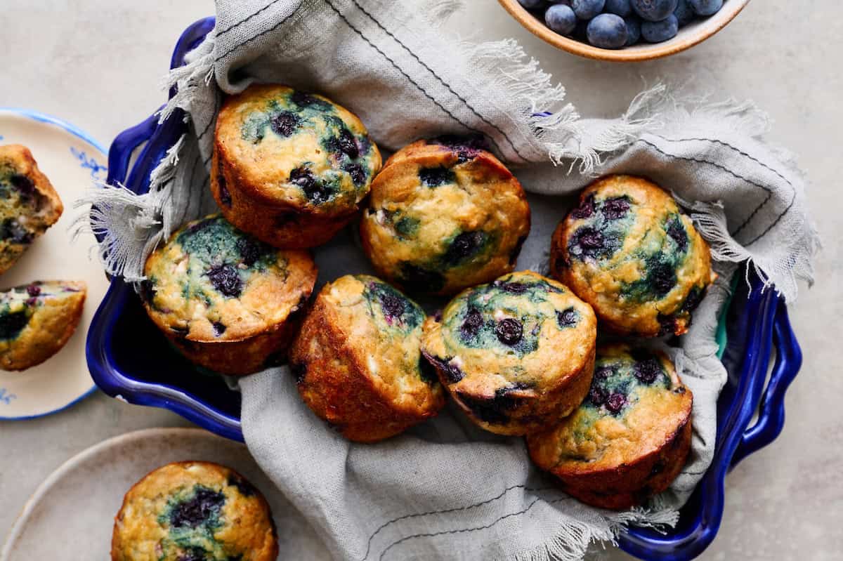 blueberry muffins made with high protein cottage cheese nestled in a blue serving tray with fresh blueberries